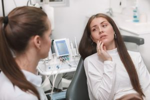 young brunette woman experiencing dental pain talks to dentist