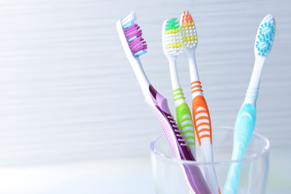 different colored tooth brushes in a glass on white countertop