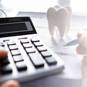 Calculator, dental implant cost estimate, and tooth model representing financing and insurance options