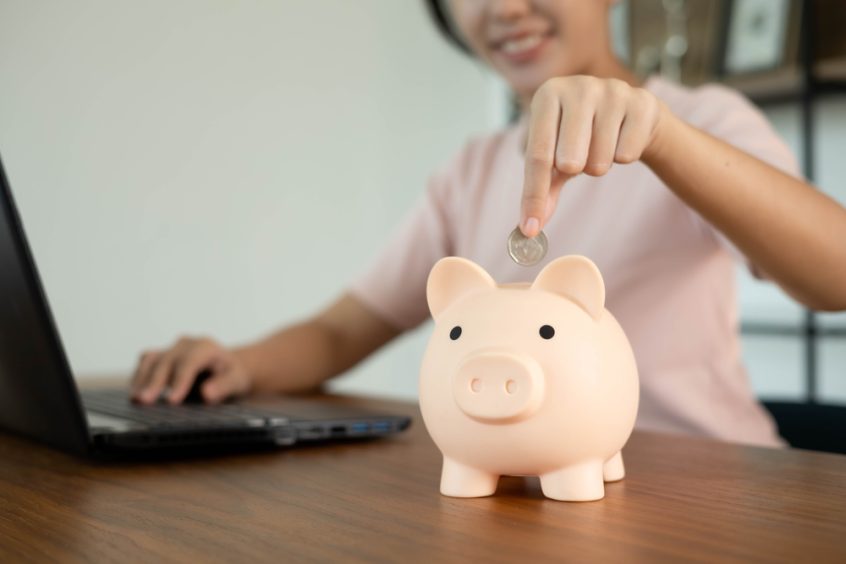 woman wearing pink shirt puts money in piggy bank