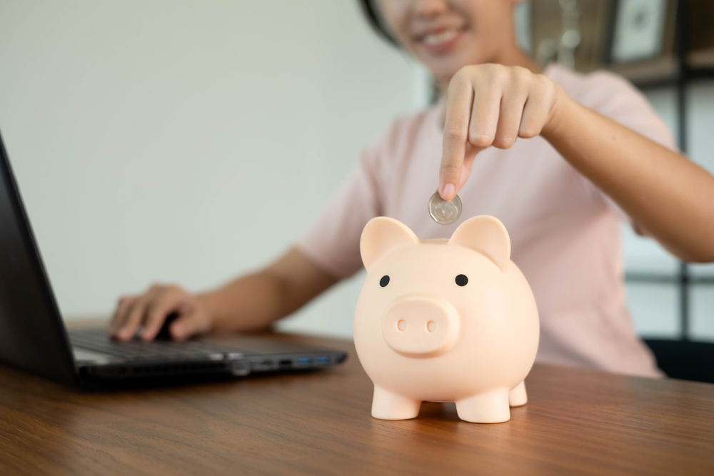 woman wearing pink shirt puts money in piggy bank